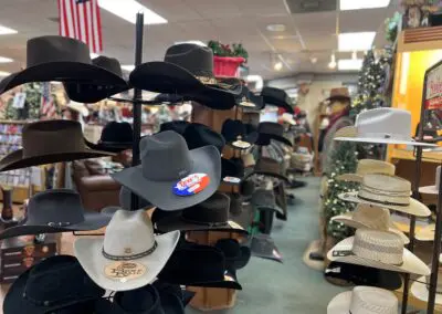 Display of assorted cowboy hats on rotating racks inside a western gift shop, rows of black, gray, tan and white felt and straw hats with price tags and an American flag in the background